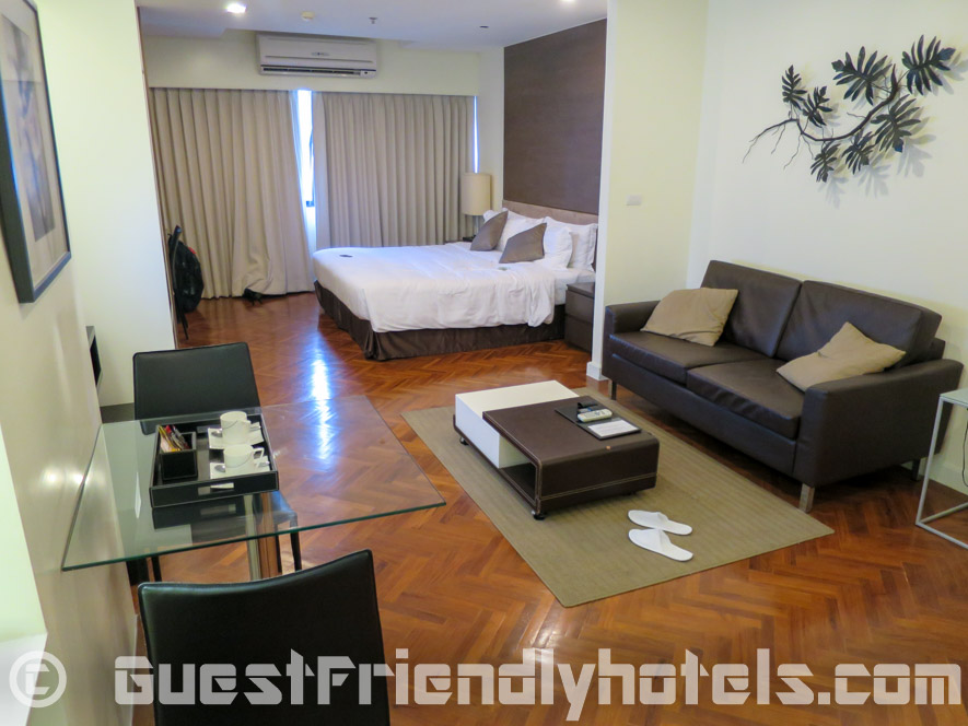 Small dining table with living room and bed in the back at Phachara Suites